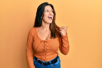 Beautiful hispanic woman wearing casual clothes pointing thumb up to the side smiling happy with open mouth