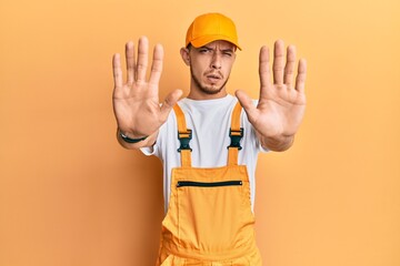 Hispanic young man wearing handyman uniform doing stop gesture with hands palms, angry and frustration expression