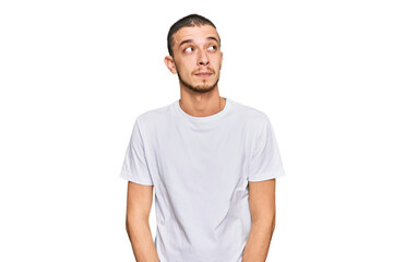 Hispanic young man wearing casual white t shirt smiling looking to the side and staring away thinking.