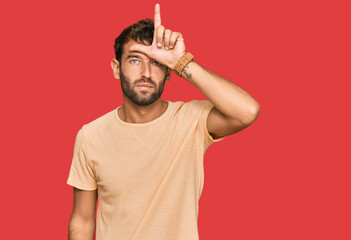 Handsome young man with beard wearing casual tshirt making fun of people with fingers on forehead...