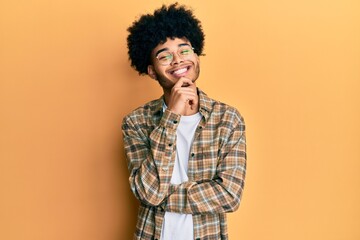Fototapeta na wymiar Young african american man with afro hair wearing casual clothes smiling looking confident at the camera with crossed arms and hand on chin. thinking positive.