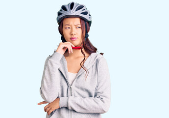 Young beautiful chinese girl wearing bike helmet serious face thinking about question with hand on chin, thoughtful about confusing idea