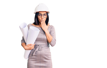 Young beautiful latin woman wearing architect hardhat and glasses holding blueprints covering mouth with hand, shocked and afraid for mistake. surprised expression