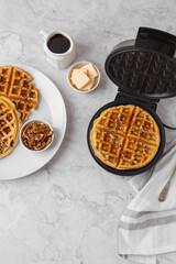 Homemade Pecan Waffles on a White Plate; One Still in Waffle Iron; White Countertop; Butter and...