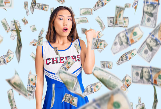 Young beautiful chinese girl wearing cheerleader uniform surprised pointing with hand finger to the side, open mouth amazed expression.