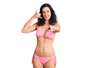Fototapeta premium Young beautiful hispanic woman wearing bikini smiling doing talking on the telephone gesture and pointing to you. call me.