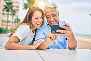 Middle age couple in love sitting at the terrace of coffee shop using smartphone happy and cheerful together