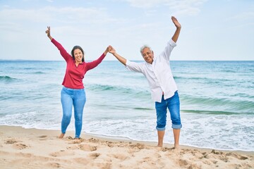 Middle age hispanic couple breathing with arms raised at the beach.