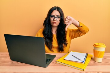 Beautiful brunette young woman working at the office wearing glasses with angry face, negative sign...