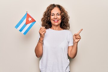 Middle age beautiful tourist woman holding cuban flag over isolated white background smiling happy...