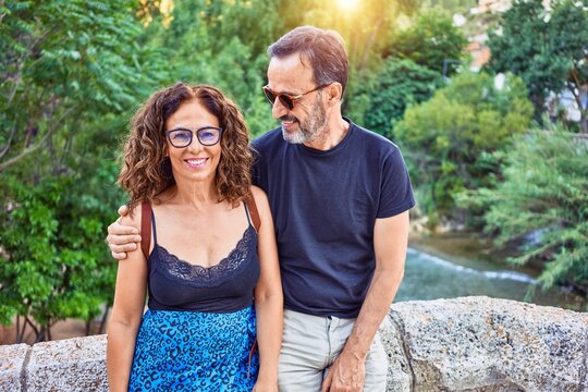 Middle age couple smiling happy sitting on stone wall looking at the camera at park
