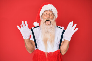 Fototapeta na wymiar Old senior man wearing santa claus costume with suspenders sticking tongue out happy with funny expression.
