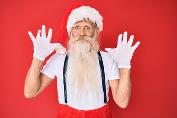 Fototapeta na wymiar Old senior man with grey hair and long beard wearing white t-shirt and santa claus costume showing and pointing up with fingers number ten while smiling confident and happy.