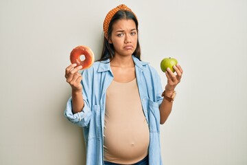 Beautiful hispanic woman expecting a baby, holding food depressed and worry for distress, crying...