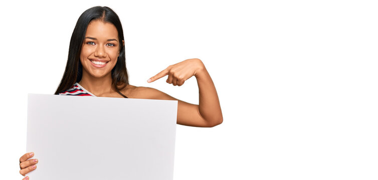 Beautiful hispanic woman holding blank empty banner pointing finger to one self smiling happy and proud
