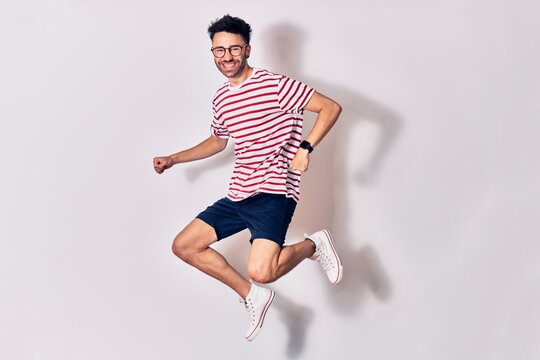 Young handsome man wearing casual clothes and glasses smiling happy. Jumping with smile on face doing winner sign with fists up over isolated white background