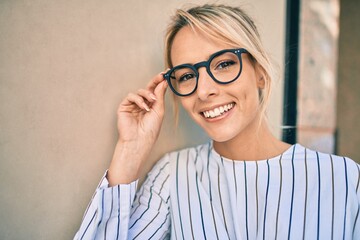 Fototapeta premium Young blonde businesswoman smiling happy leaning on the wall at the city.