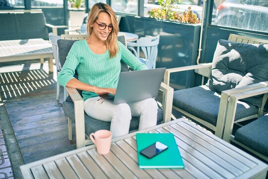 Young blonde woman smiling happy working using laptop sitting at the coffee shop terrace.