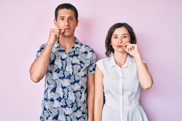 Beautiful couple wearing casual clothes mouth and lips shut as zip with fingers. secret and silent,...