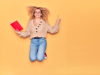 Young beautiful curly student girl wearing glasses smiling happy. Jumping with smile on face...