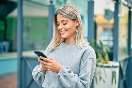 Young blonde girl smiling happy using smartphone at the city