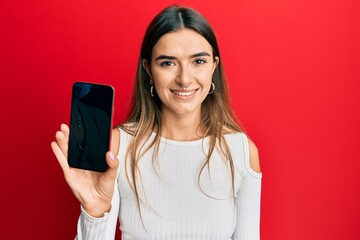 Young hispanic woman holding smartphone showing blank screen looking positive and happy standing and smiling with a confident smile showing teeth