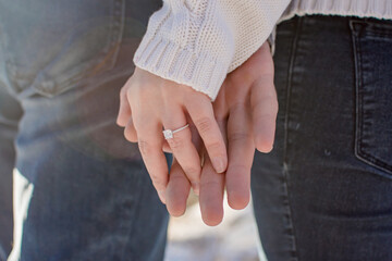 Hands with a diamond engagement ring close up from behind, couple wearing jeans holding hands