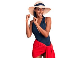 Young african american woman wearing swimsuit and summer hat pointing to the back behind with hand and thumbs up, smiling confident