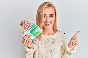 Beautiful caucasian woman holding norwegian krone banknotes smiling happy pointing with hand and finger to the side