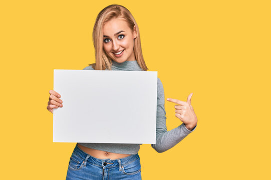 Beautiful caucasian woman holding blank empty banner smiling happy pointing with hand and finger