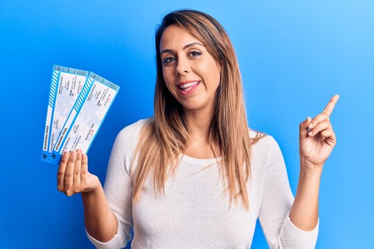 Young beautiful woman holding airline boarding pass smiling happy pointing with hand and finger to the side