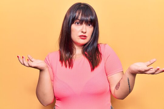 Young plus size woman wearing casual clothes clueless and confused expression with arms and hands raised. doubt concept.