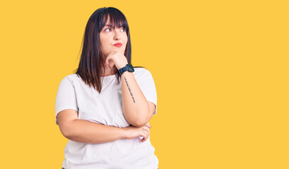 Young plus size woman wearing casual clothes with hand on chin thinking about question, pensive...
