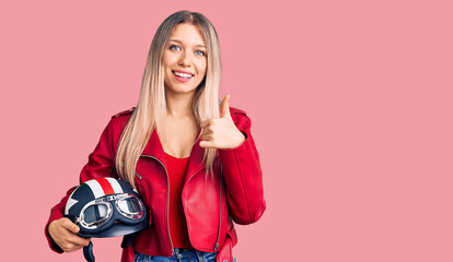 Fototapeta na wymiar Young beautiful blonde woman holding motorcycle helmet smiling happy and positive, thumb up doing excellent and approval sign