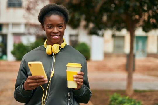 Young african american girl drinking coffee using smartphone and headphones at the city