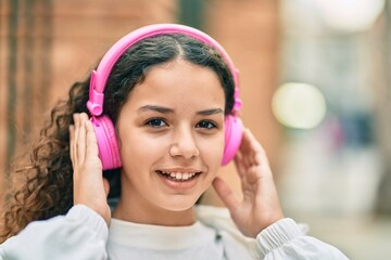 Hispanic child girl smiling happy using headphones at the city.