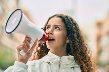 Hispanic child girl shouting angry using megaphone at the city.