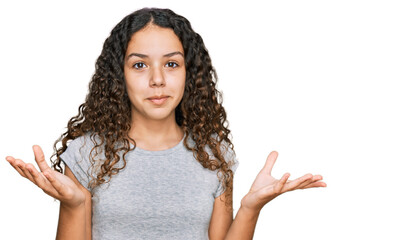 Teenager hispanic girl wearing casual clothes clueless and confused expression with arms and hands...