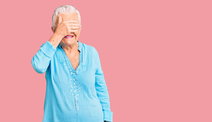 Senior beautiful woman with blue eyes and grey hair wearing summer dress smiling and laughing with hand on face covering eyes for surprise. blind concept.