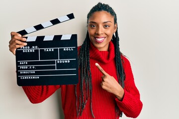 African american woman with braids holding video film clapboard smiling happy pointing with hand...