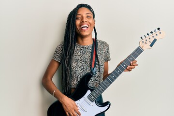 African american woman playing electric guitar smiling and laughing hard out loud because funny...