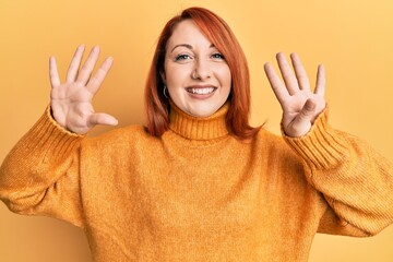 Beautiful redhead woman wearing casual winter sweater over yellow background showing and pointing...