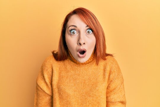 Beautiful redhead woman wearing casual winter sweater over yellow background afraid and shocked with surprise and amazed expression, fear and excited face.