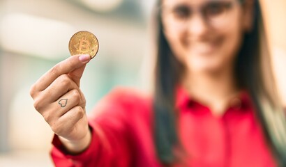 Young hispanic woman smiling happy holding bitcoin at the city.