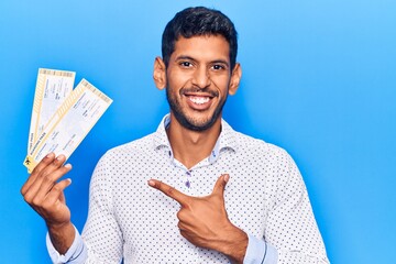 Young latin man holding boarding pass smiling happy pointing with hand and finger