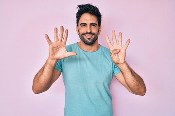 Fototapeta premium Handsome hispanic man with beard wearing casual clothes showing and pointing up with fingers number nine while smiling confident and happy.