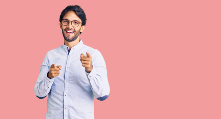 Handsome hispanic man wearing business shirt and glasses pointing fingers to camera with happy and funny face. good energy and vibes.