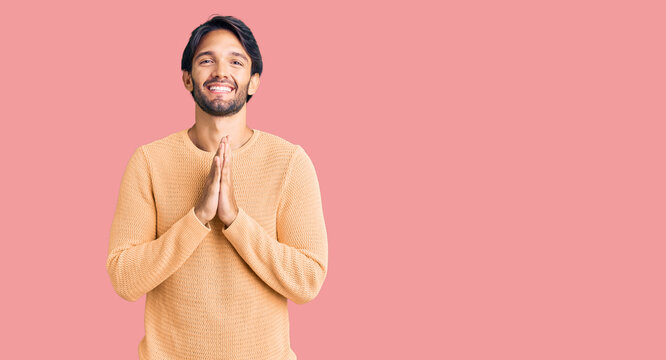 Handsome hispanic man wearing casual sweater praying with hands together asking for forgiveness smiling confident.