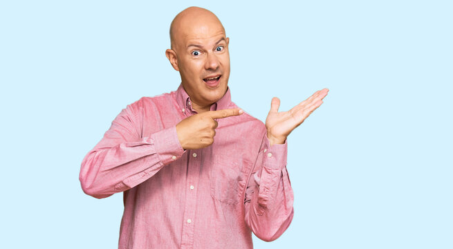 Middle age bald man wearing casual clothes amazed and smiling to the camera while presenting with hand and pointing with finger.