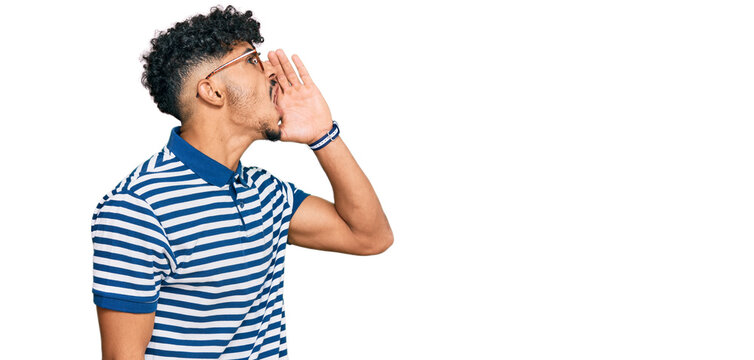 Young arab man wearing casual clothes and glasses shouting and screaming loud to side with hand on mouth. communication concept.